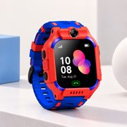 A kids' smartwatch with a bright red and blue protective case and matching strap, shown on a clean white surface with a light blue box in the background.